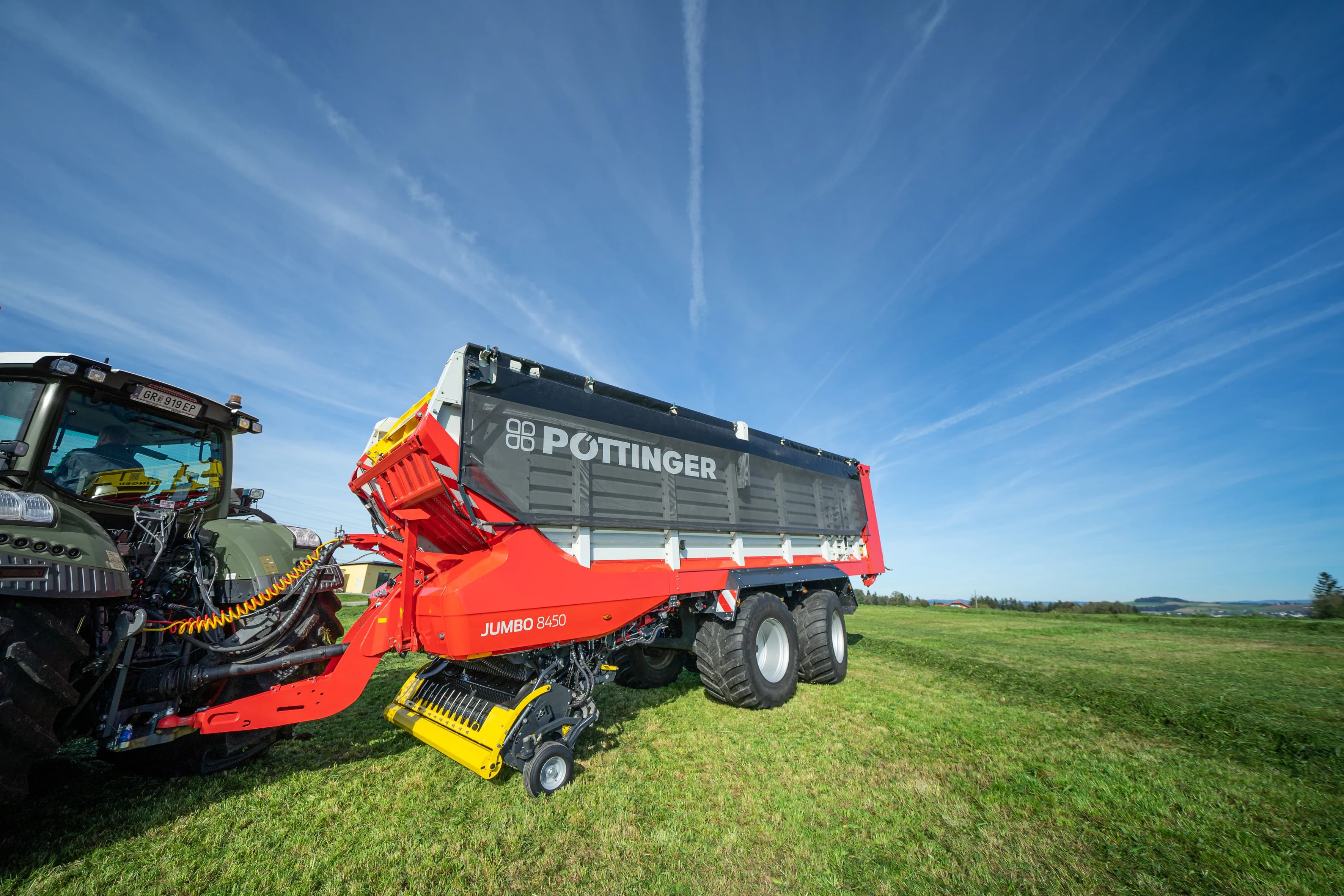 Sběrací vůz PÖTTINGER JUMBO 8450 připojený k traktoru na louce